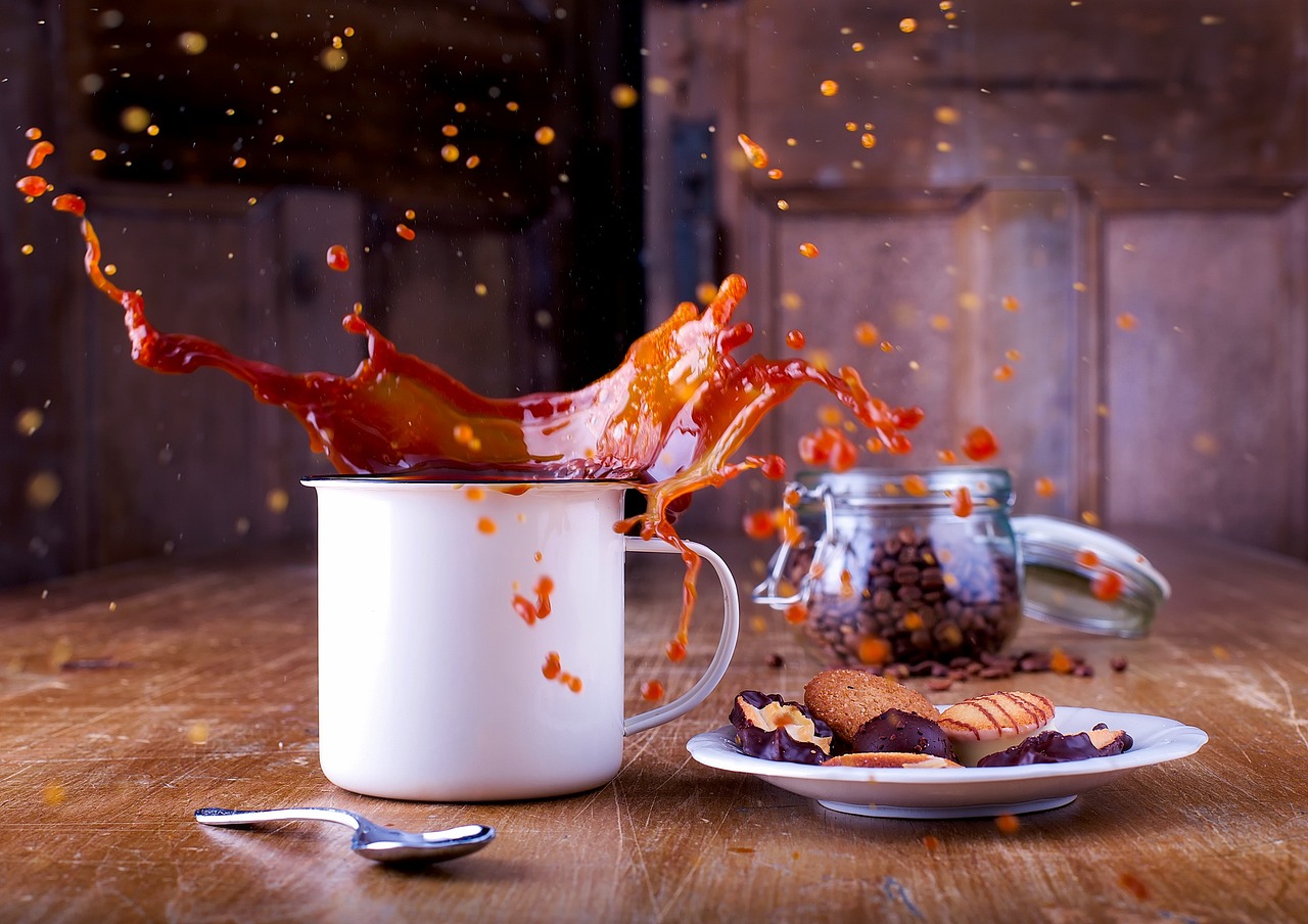 Coffee splashing out of a cup sitting on a able with a plate of cookies